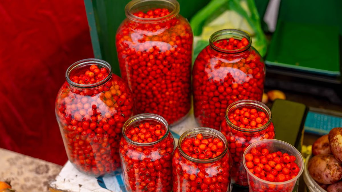Colorful assortment of bright red berries stored in glass jars on a market stall table.